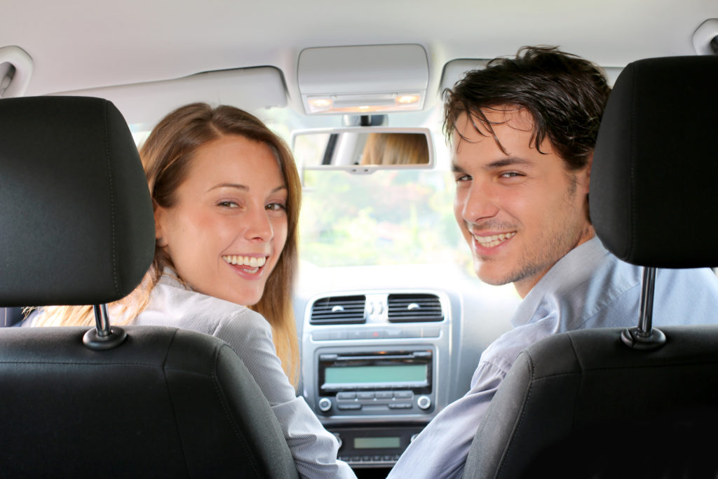 pair of happy white people in the front seat of a car, save on car insurance